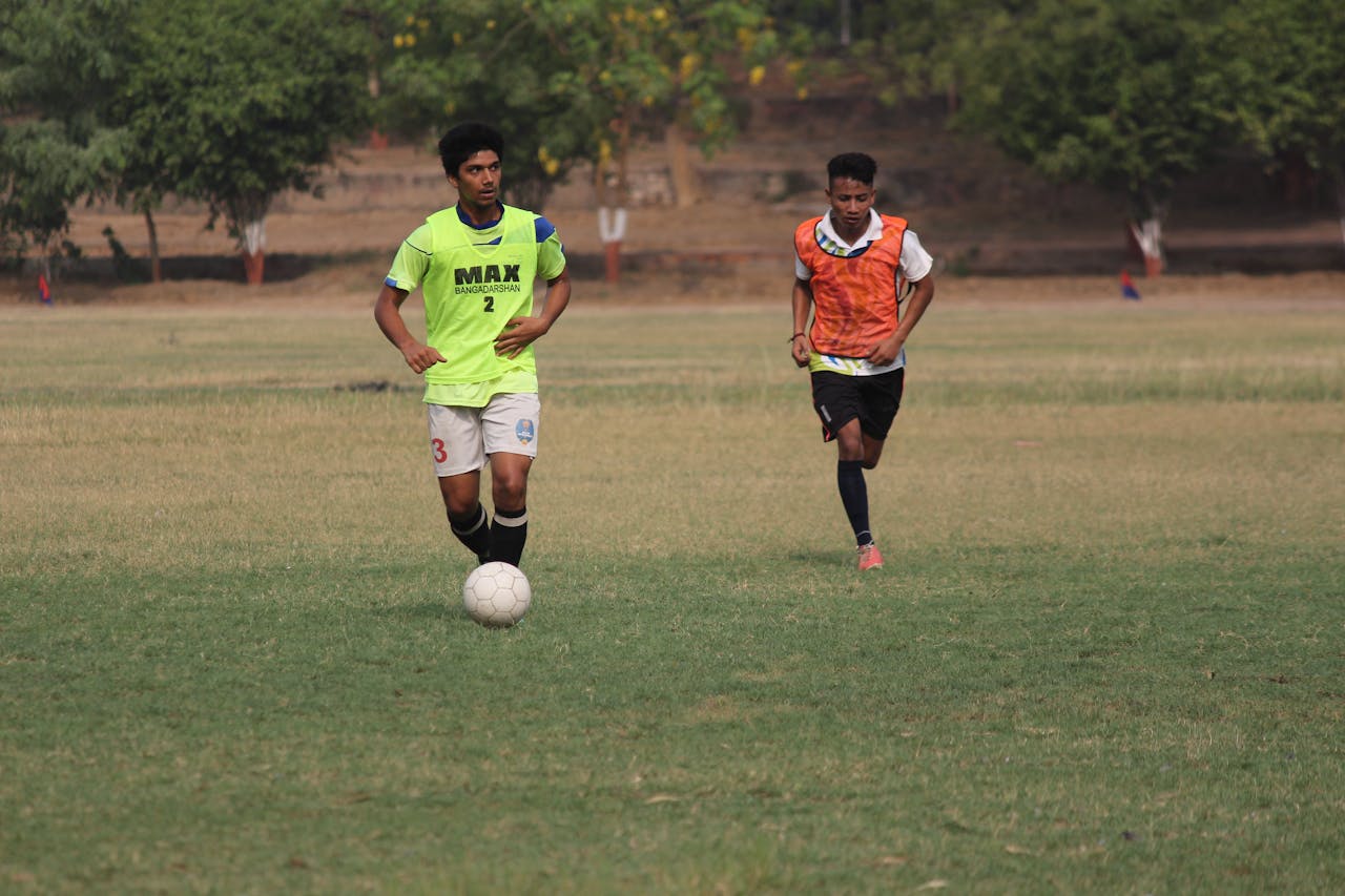 Two soccer players practicing on an outdoor field, wearing sports uniforms.